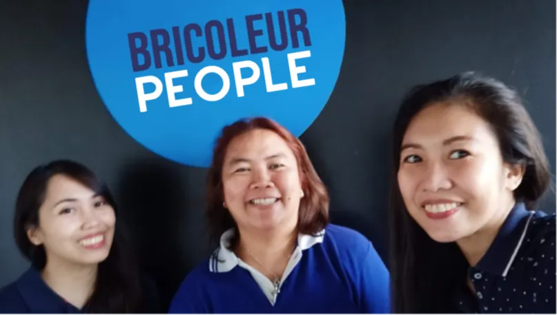 Three smiling Bricoleur People team members standing in front of a Bricoleur People branded backdrop